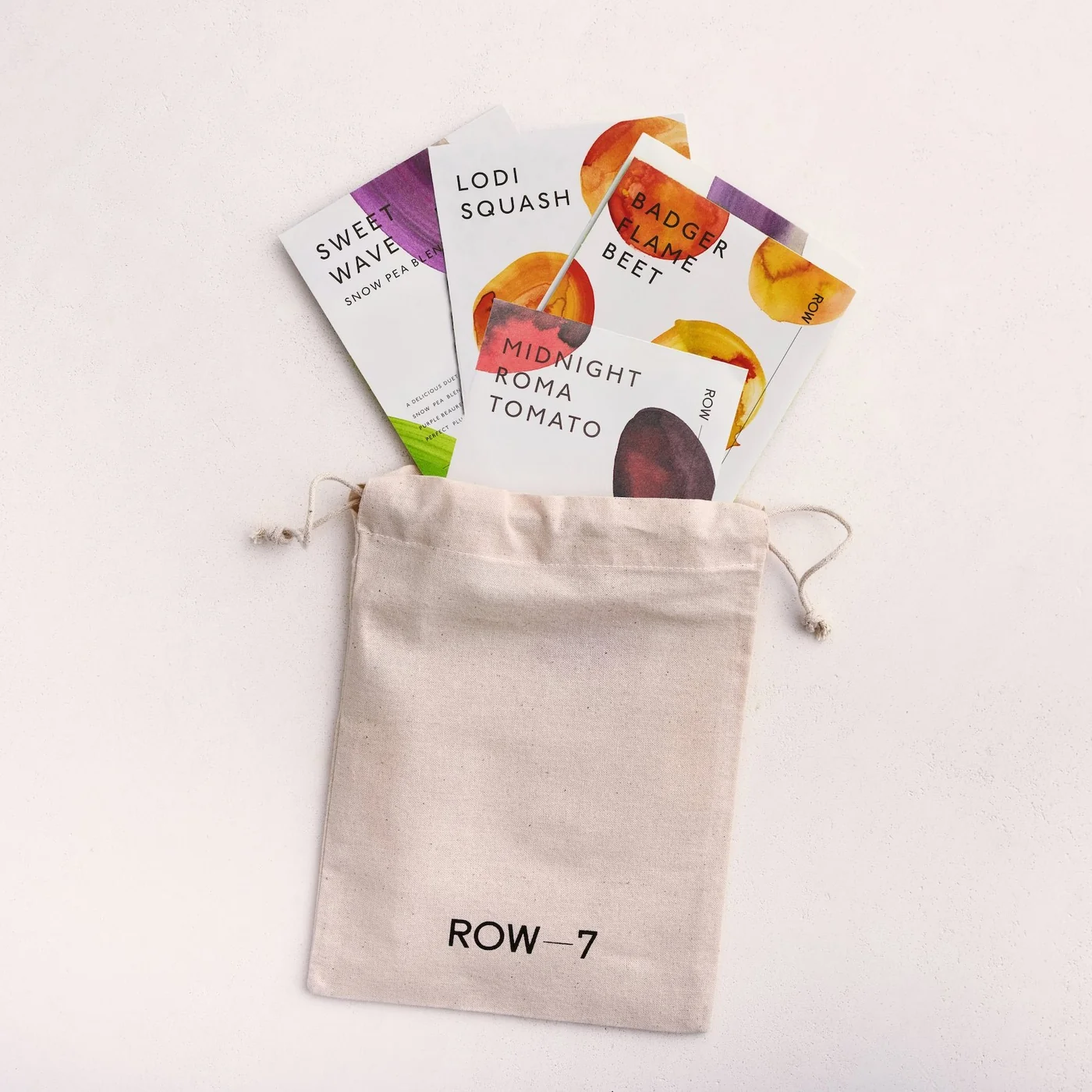 Row 7 Seed Company organic culinary seed packets including Badger Flame Beet, Midnight Roma Tomato, Sweet Wave Snow Pea, and Lodi Squash in canvas drawstring pouch